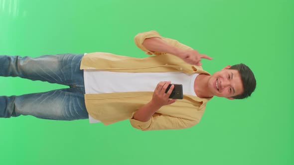 Asian Man Flipping Through The Mobile Phone With A Smile Pointing Up In Green Screen Studio