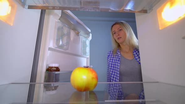 The woman opens the refrigerator, in which there is only an apple. She's upset.
