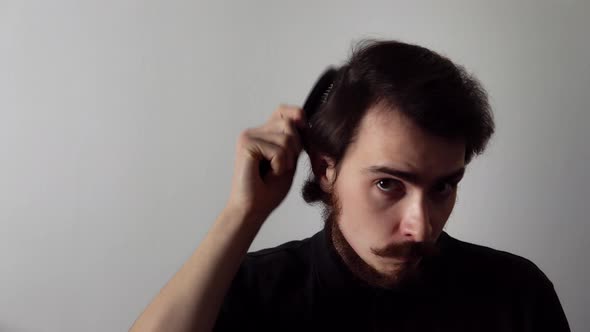 Young Caucasian Man is Combing His Hair By Brush Standing on a White Background and Smiling