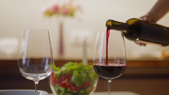 Woman Fills Wineglass with Red Wine Serving Romantic Supper