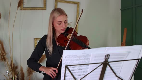 Young Blonde Woman Playing Violin By Notes