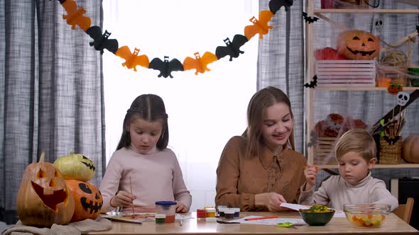 A Family in a Room Decorated for Halloween is Sitting at a Table on Which There are Pumpkins and