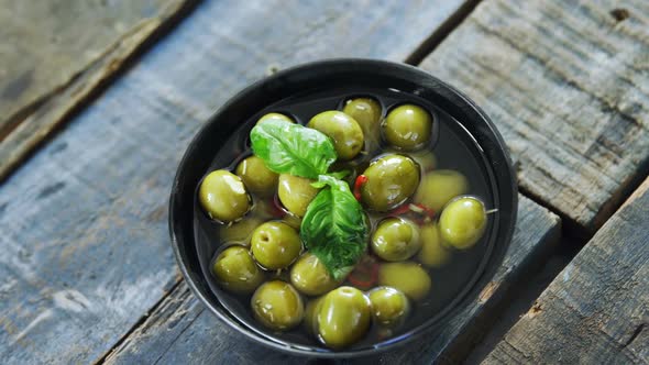 Bowl of green olives in vinegar garnished with herb