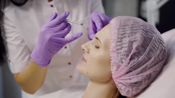 An experienced cosmetologist makes botox in the eyebrow area for a woman.