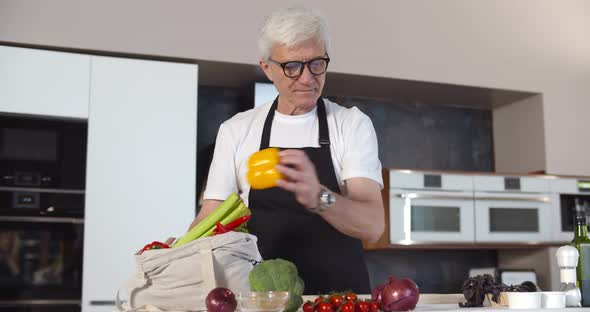 Happy Senior Man Unpacking Grocery Bag with Vegetables Cooking in Modern Kitchen