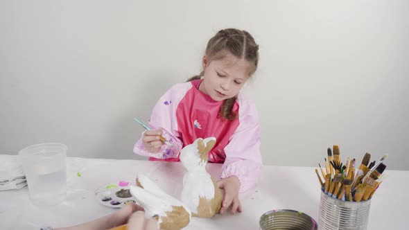 Little girl painting paper mache figurine at homeschooling art class.