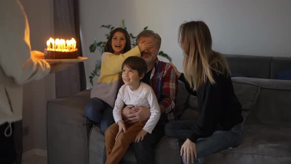 Happy Grandfather with Closed Eyes Blowing Candles on Birthday Cake with His Family