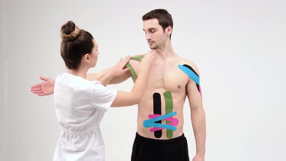 The doctor glues a special treatment tape to mail shoulder. Physiotherapist sticks kinesio tapes