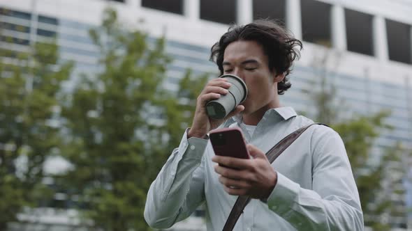 Asian Man Drinking Coffee and Using Mobile on Street