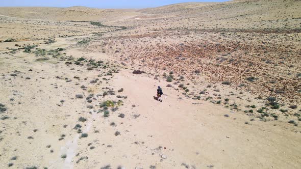 Aerial orbit and fly over of hiker on desert trail showing wilderness landscape on sunny day with bl