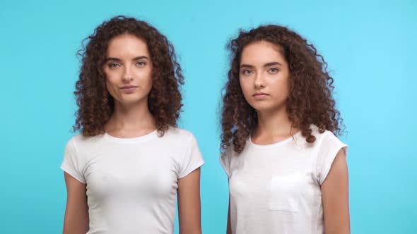 One Beautiful Caucasian Twin with Curly Hair Wearing White Tshirt Showing Ok While Another Removing