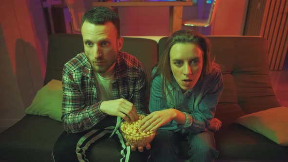 A Shocked Young Couple with Popcorn Is Watching a Tv Program at Night