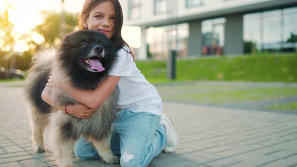 Brunette Girl Hugs a Fluffy Dog at Sunset Outdoors