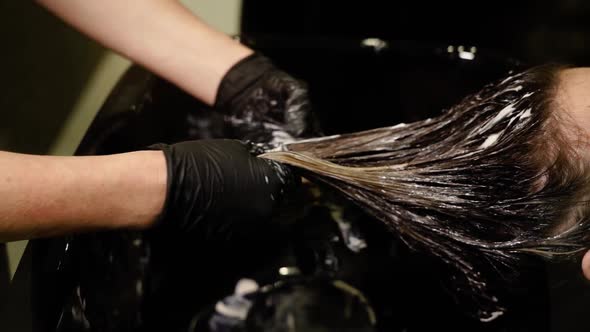 Woman in Black Gloves Spreads Lotion on Lady Long Hair