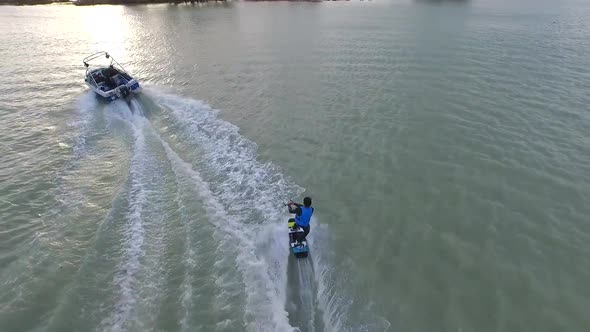 Aerial shot of young man wake boarding behind a motorboat in a lake.