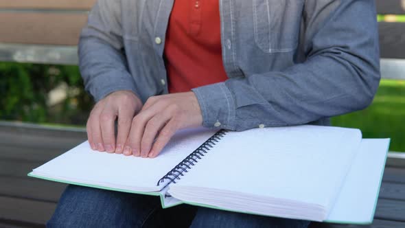 Blind Man Reading Braille Book Sitting on Bench in Summer Park