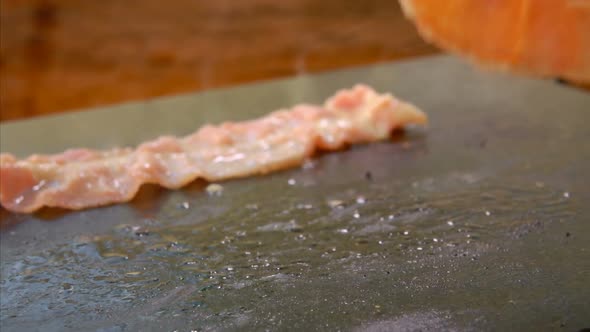 Cook Turns Bacon with Metal Tongs on the Grill