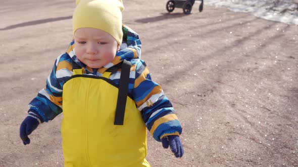 Child in Yellow Waterproof Rain Pants Bibs for Kids Learning to Walk on Footpath in Cold Season