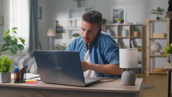 Young Businessman Talking on a Smartphone at a Workplace at Home in the Living Room