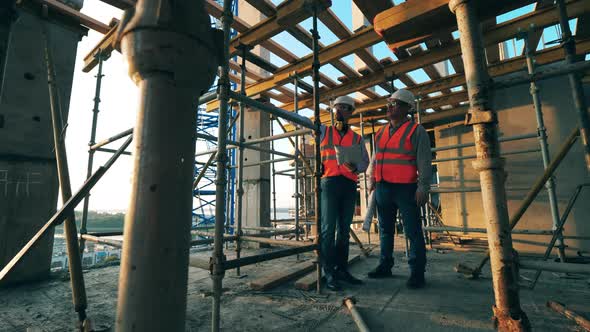 Two Engineers Are Having a Discussion Construction Plan Among the Scaffolding