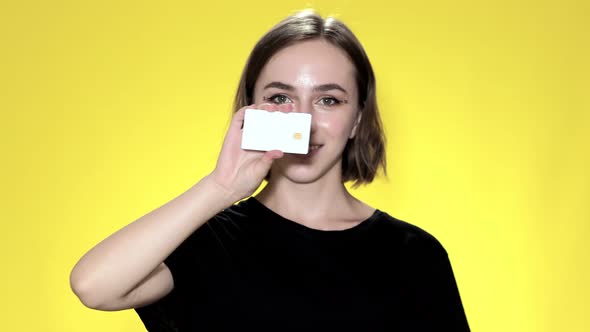 Smiling young woman holding credit card on yellow background