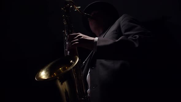 Male Saxophonist Dressed in a Classic Suit Blows a Saxophone in the Dark of Studio