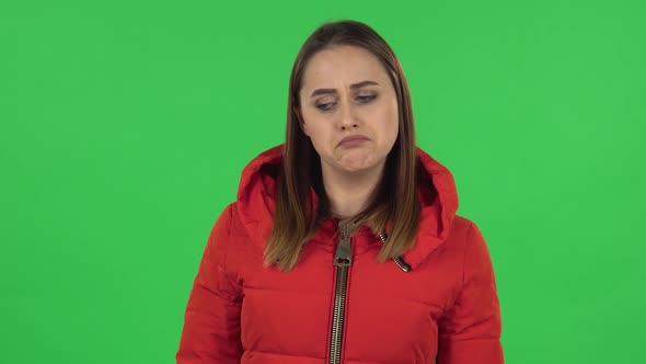 Portrait of Lovely Girl in a Red Down Jacket Upset and Shrugging. Green Screen