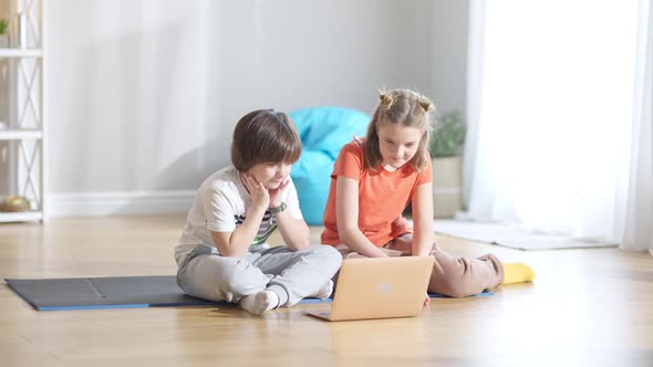 Portrait of Relaxed Caucasian Children Sitting at Home with Laptop Talking