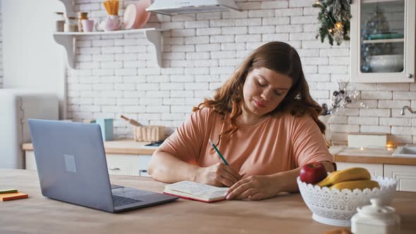 Overweight Lady Making Notes Looking at Computer Screen Writing New Nutrition and Dieting Plan at