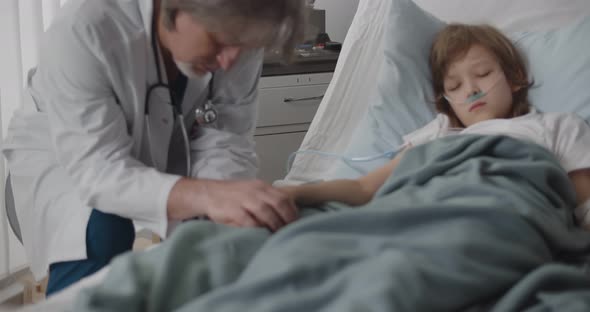 Aged Pediatrician Holding Sick Kid Hands and Sleeping at Bedside