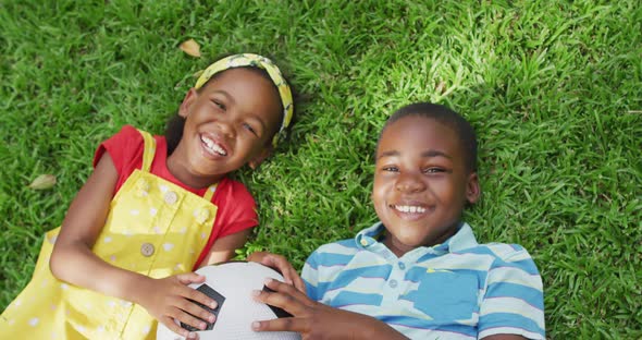 Animation of happy african american siblings lying on lawn and holding ball