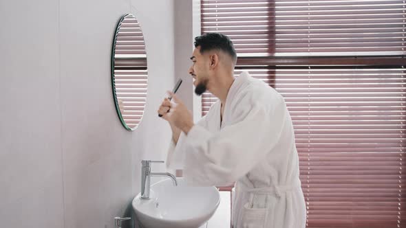 Side View Carefree Funny Arabic Hispanic Indian Man Bearded Guy in White Bathrobe Standing at Home
