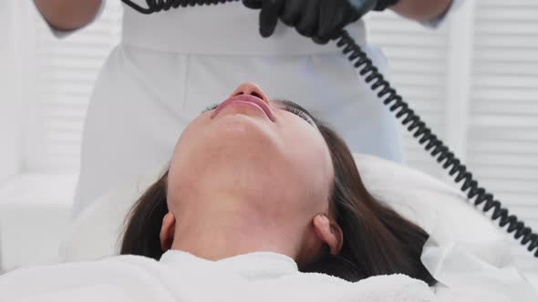 Young Brunette Woman Getting Facials  Therapist Using Light Device on Her Skin