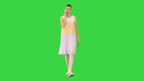 Young Beautiful Girl in Whiteyellow Dress Walks Talking on Mobile Phone on a Green Screen Chroma Key
