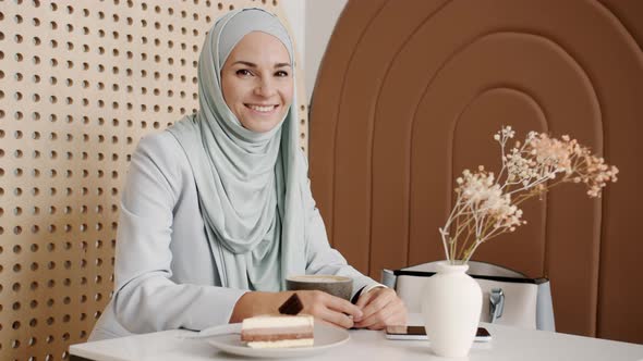 Slow Motion Portrait of Charming Woman in Hijab Smiling Sitting at Table with Food and Drink in