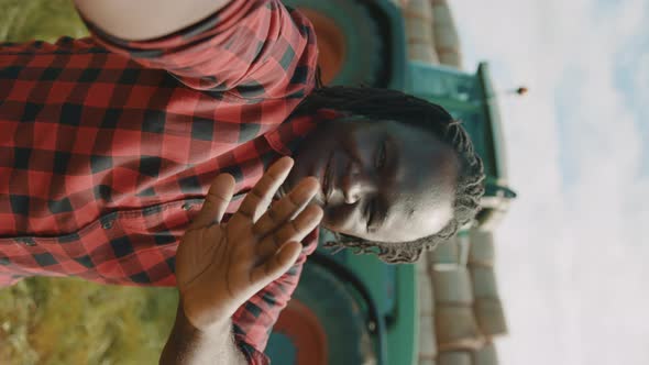 Video Call. African Farmer Waving To the Smartphone Camere in Front of the Tractor. Vertical Shot