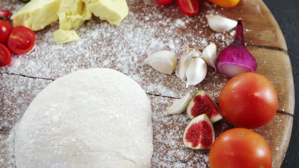 Rolling pin with pizza dough, flour, vegetables and spices on plate