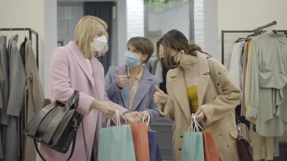 Middle Shot of Confident Young Women in Covid-19 Face Masks Looking at Purchases in Shopping Bags