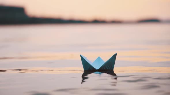 Nice paper boat on evening water surface. One blue origami ship sailing in the river calmly