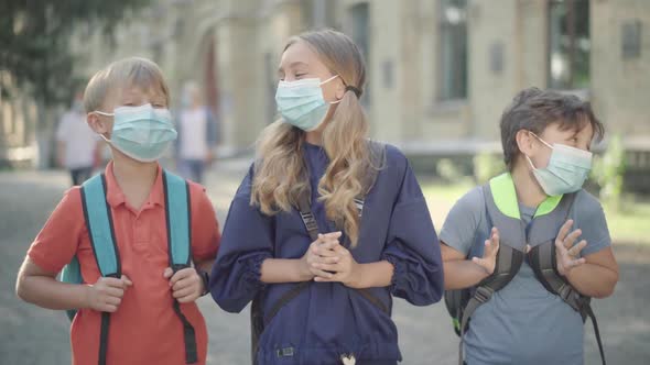 Positive Caucasian Pupils in Face Masks Posing Outdoors As Blurred High-school Students Passing at