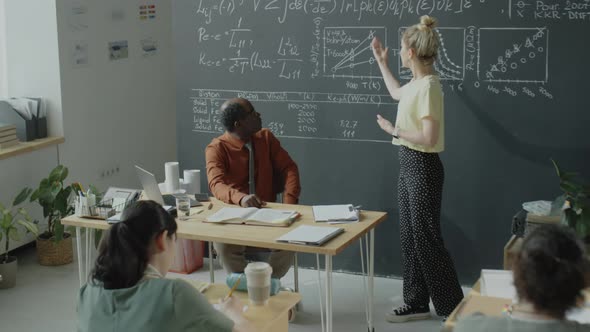 Female Student Explaining Formulas on Chalkboard