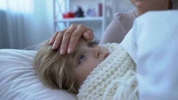 Caring Mom Touching Forehead Little Ill Daughter Wrapped in Scarf and Lying Bed