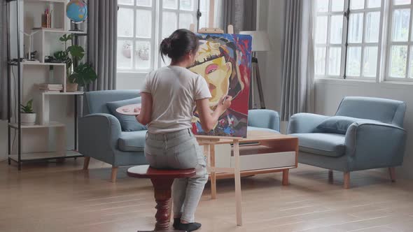 Hind View Of An Asian Artist Girl Coming To Sit And Holding Paintbrush Painting A Girl On The Canvas