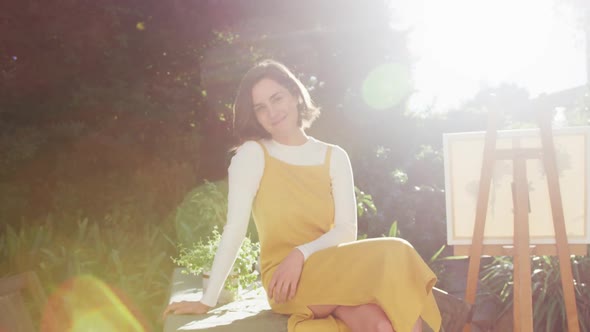 Portrait of smiling caucasian woman with brown hair painting in sunny garden