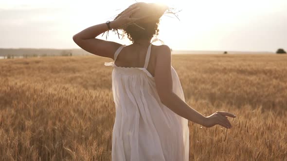 Young Woman Running in the Wheat Field While Holding Her Straw Hat