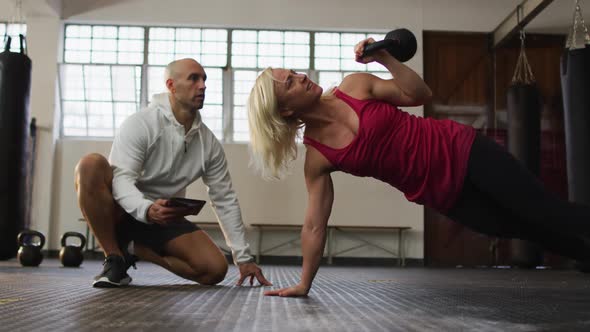 Fit caucasian woman working out with kettle bell with male trainer at the gym