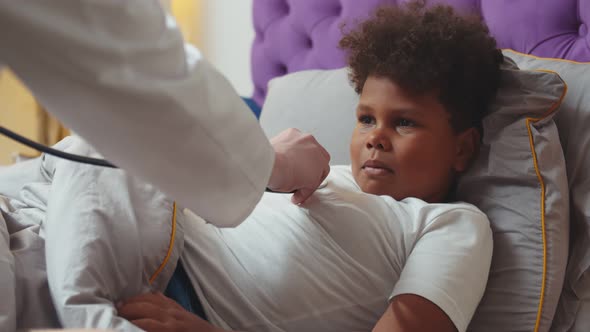 Doctor with Stethoscope Examining Sick African Kid Boy During Home Visit