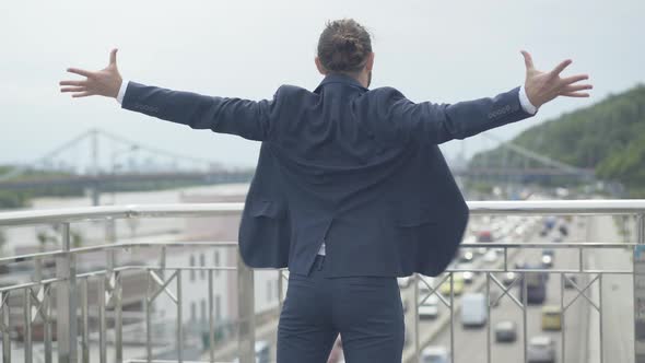 Back View of Cheerful Businessman Standing on Urban City Bridge and Stretching Hands in Joy. Young