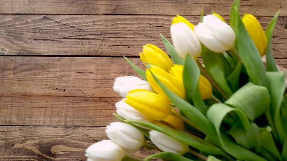 Put yellow and white tulips bouquet on a wooden table top view