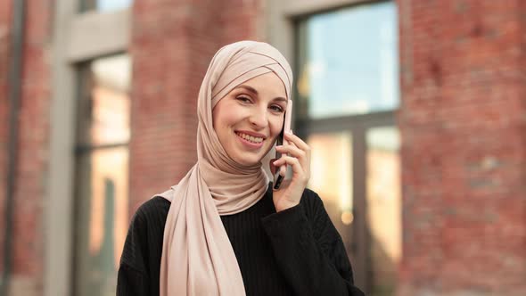 Smiling Muslim Woman Wearing Trendy Black Suit Walking in City Street and Uses Her Phone